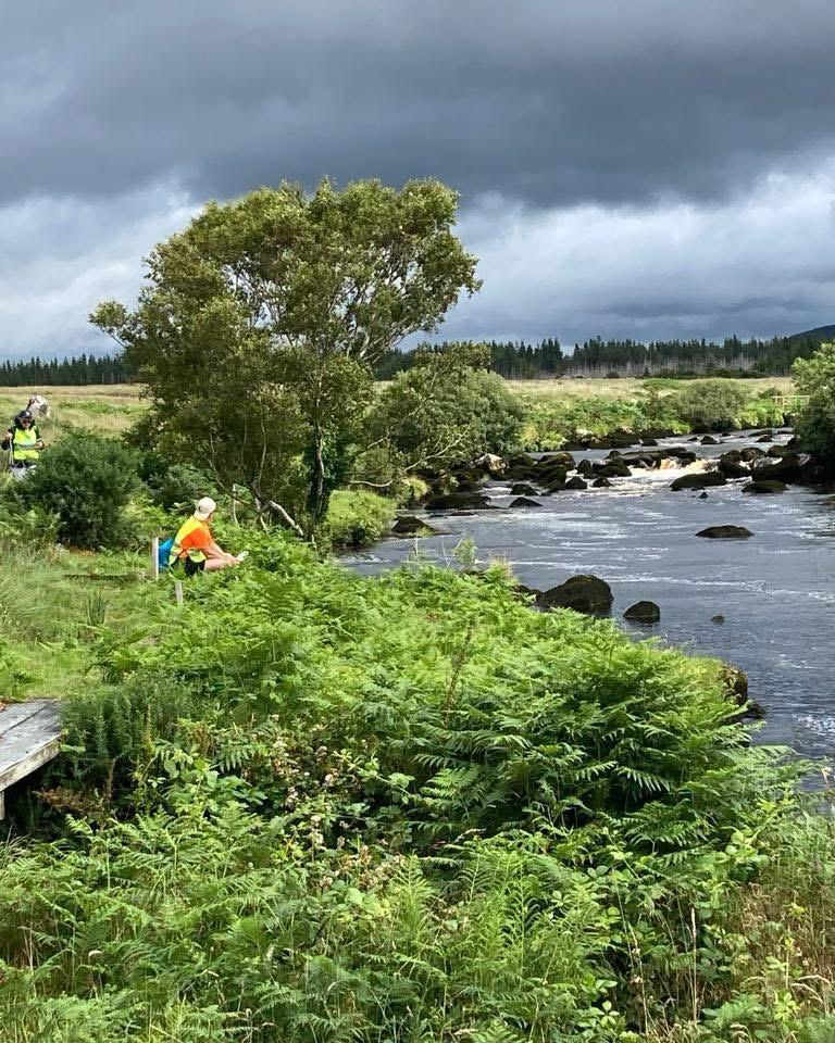 A walker sits on the banks of the Ownea River between Ardara and Glenties, County Donegal, Ireland.